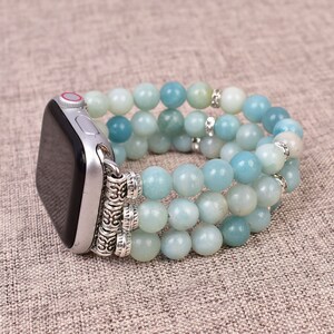 May include: A light blue beaded Apple Watch band with silver accents. The band is made of three rows of beads and has a silver clasp.