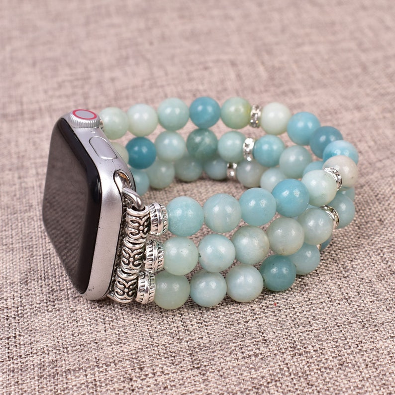May include: A light blue beaded Apple Watch band with silver accents. The band is made of three rows of beads and has a silver clasp.