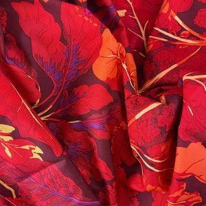 May include: Red fabric with a floral pattern featuring large, stylised leaves in shades of red, orange, and purple. The fabric has a textured, slightly wrinkled appearance.