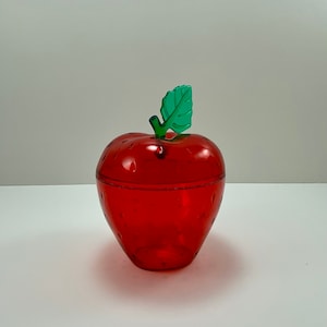 Op de afbeelding: Een rode plastic container in de vorm van een aardbei met een groen plastic blad erop.