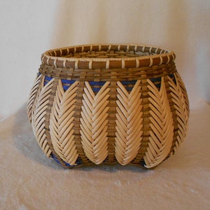 May include: A woven basket with a brown and white pattern and blue accents. The basket has a rounded shape and a wide opening.