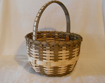 May include: A woven basket with a brown and white pattern and a wooden handle. The basket is round and has a wide opening.