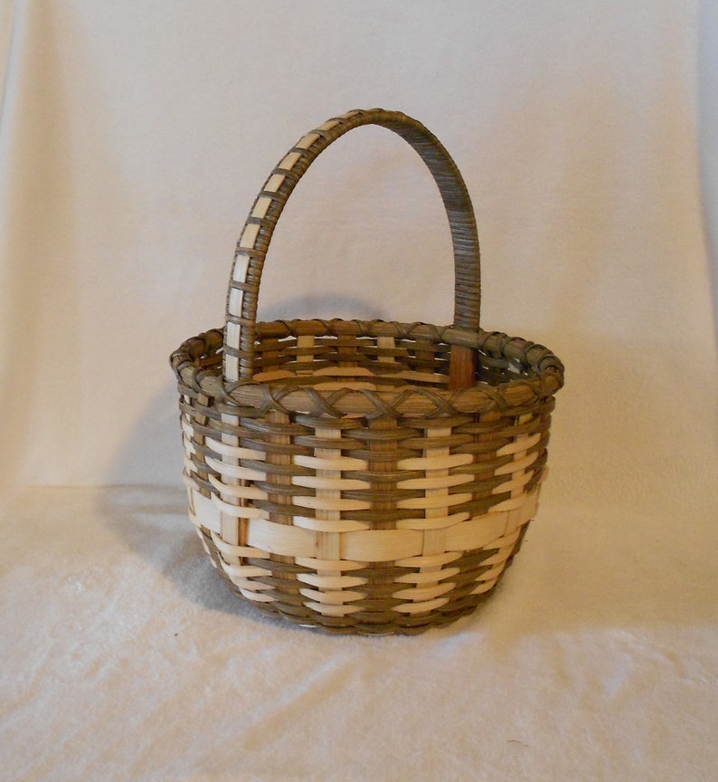 May include: A woven basket with a brown and white pattern and a wooden handle. The basket is round and has a wide opening.