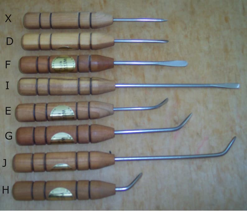 Op de afbeelding: Set van negen leerbewerkingstools met houten handvatten en metalen punten. De tools hebben verschillende vormen en maten. De tools zijn gelabeld met de letters X, D, F, I, E, G, J en H.