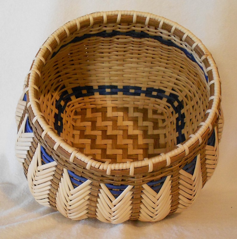 Puede incluir: Una cesta tejida con un patr&oacute;n marr&oacute;n y blanco y detalles azules. La cesta es redonda y tiene una abertura ancha.