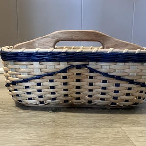 May include: A woven basket with a wooden handle. The basket is made of natural wicker and has a blue and white striped pattern.