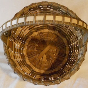 May include: A woven basket with a light brown handle and a natural brown body. The basket is made of natural materials and has a circular shape.