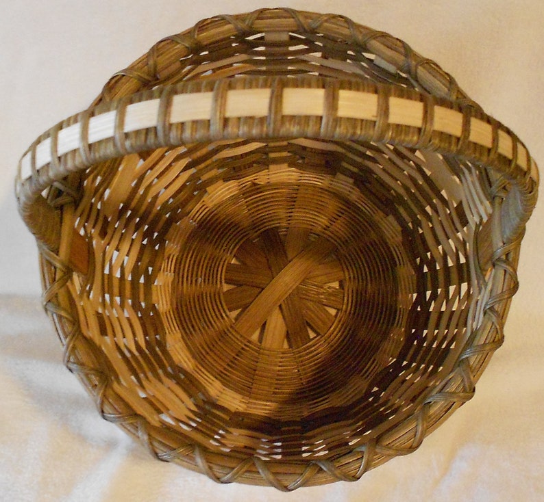 May include: A woven basket with a light brown handle and a natural brown body. The basket is made of natural materials and has a circular shape.