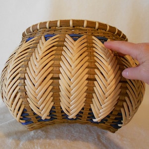 Puede incluir: Una cesta tejida con un patr&oacute;n de espiga en colores naturales y azules. La cesta es redonda y tiene una abertura ancha.