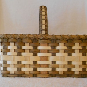 May include: A woven basket with a brown and white chequered pattern. The basket has a single handle and is made of natural materials.
