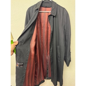 May include: A black trench coat featuring a pointed collar, long sleeves, and a button-front closure. The interior is lined with a dark red and black vertical striped fabric. A black label with the text Towncraft is visible on the inner front.