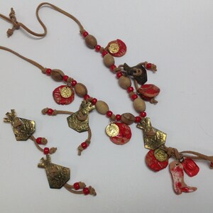 May include: A brown leather necklace with red beads and gold charms. The charms are shaped like houses and have a rustic, handmade look. The necklace is a unique and stylish piece of jewelry.