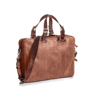 May include: A brown leather briefcase with a top handle and an adjustable shoulder strap. The bag has a zipper closure and a metal buckle. The bag has the text "KRUK GARAGE" embossed on the front.