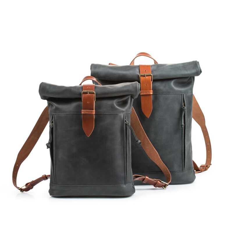 May include: Two black leather roll-top backpacks with brown leather straps and buckles.