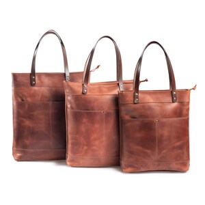 May include: Three brown leather tote bags of different sizes, all with a single pocket on the front.