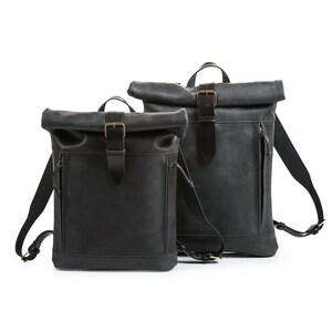 May include: Two black leather roll-top backpacks with adjustable straps and brass buckles.