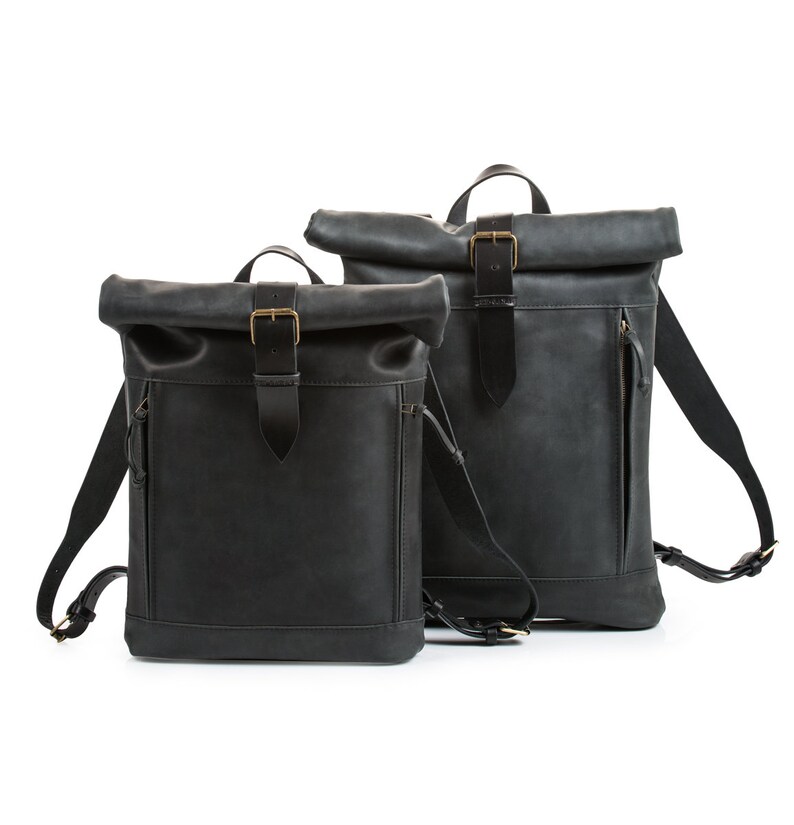 May include: Two black leather roll-top backpacks with adjustable straps and brass buckles.