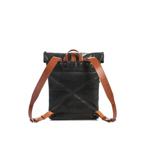 May include: Black leather backpack with brown leather straps and buckles. The backpack has a roll-top closure and a flap with the text "FRUIT CAVAN" embossed on it.
