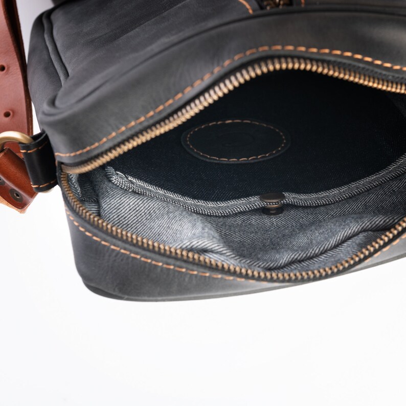May include: A black leather crossbody bag with a zipped opening and a denim lining. The bag has a brown leather strap.
