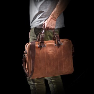 May include: A brown leather briefcase with a long strap and the text "KRUK GARAGE" embossed on the front.