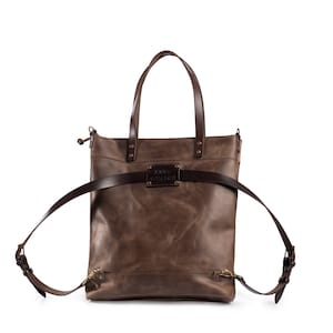 May include: A brown leather tote bag with a strap that can be worn as a backpack. The bag has a metal plate with the text "JORDI GARAGE" on it.