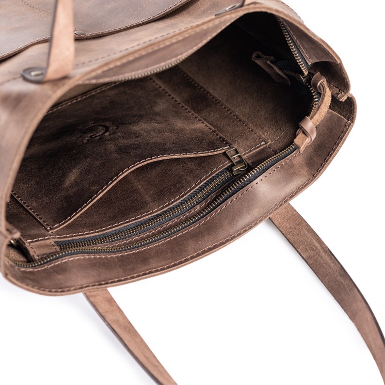 May include: Brown leather tote bag with a zippered pocket and two top handles. The bag is open and the interior is visible.