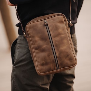May include: A brown leather crossbody bag with a zip closure. The bag has a distressed look and a worn texture.