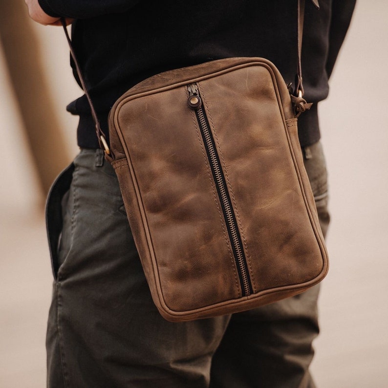 May include: A brown leather crossbody bag with a zip closure. The bag has a distressed look and a worn texture.