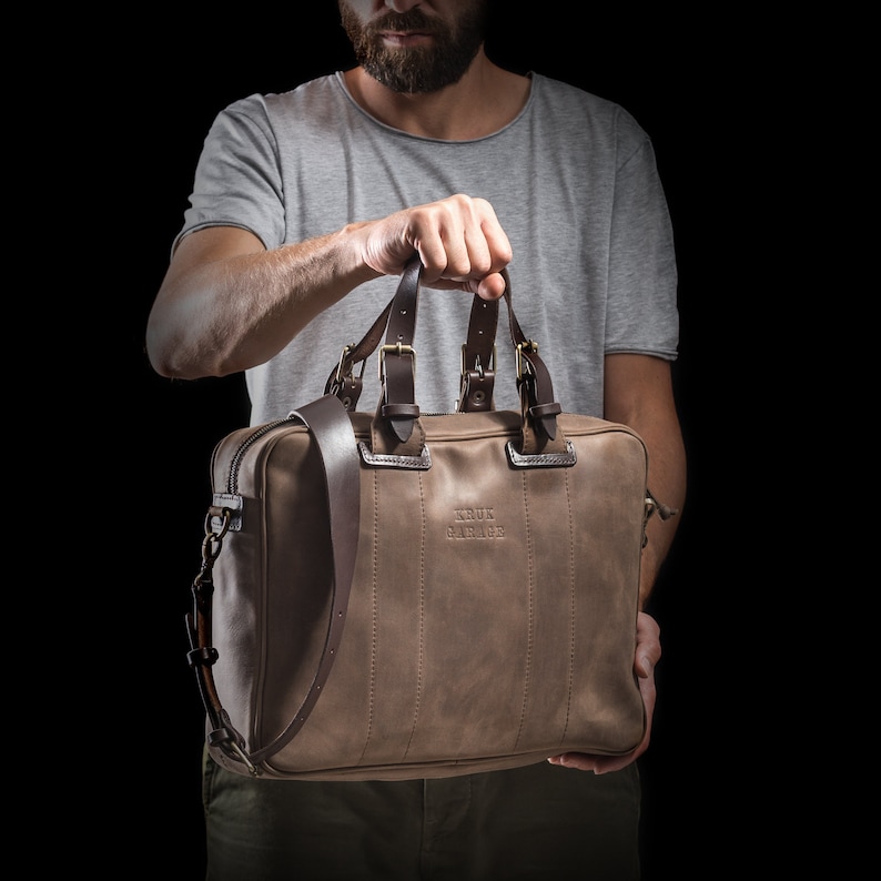 May include: A brown leather briefcase with a shoulder strap and the text "KRUK GARAGE" embossed on the front.