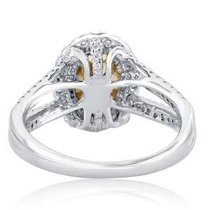 May include: A silver-toned ring featuring a split shank design adorned with small clear stones. The center setting holds a yellow stone, surrounded by a halo of clear stones, with additional clear stones embedded along the band's split arms.