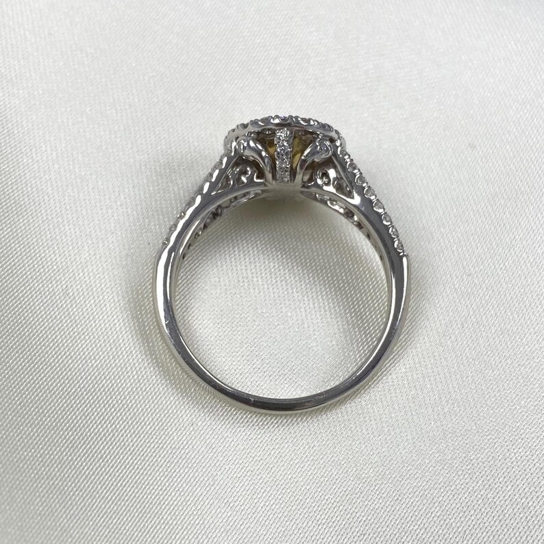 May include: A silver-toned ring featuring a central yellow stone surrounded by a halo of small clear stones. The band and setting are decorated with intricate cut-out metalwork and additional small clear stones along the shoulders.