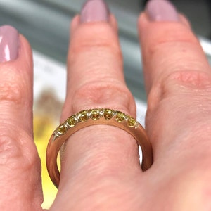 Puede incluir: Un anillo de banda de oro rosa que presenta una hilera de ocho peque&ntilde;as piedras preciosas redondas de color amarillo engastadas a lo largo de la mitad superior. El metal tiene un acabado liso y pulido, con piedras en engaste de garras.