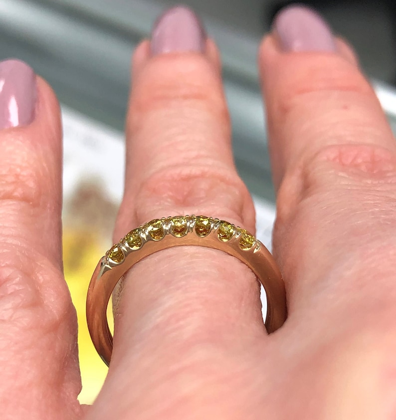 Puede incluir: Un anillo de banda de oro rosa que presenta una hilera de ocho peque&ntilde;as piedras preciosas redondas de color amarillo engastadas a lo largo de la mitad superior. El metal tiene un acabado liso y pulido, con piedras en engaste de garras.