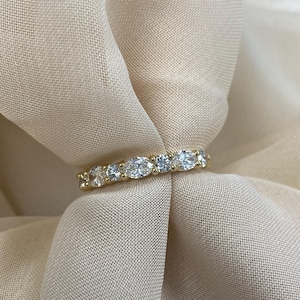 May include: A gold band ring with a row of oval-shaped clear gemstones.