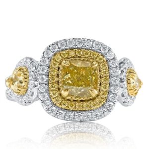 May include: A gold and white ring with a large, cushion-cut yellow diamond surrounded by smaller diamonds. The ring has a halo setting and two smaller yellow diamonds on the sides.