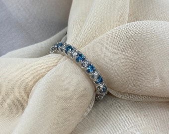 May include: A silver band ring with a row of blue and white gemstones.