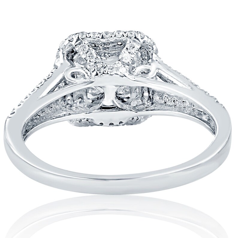 May include: A silver ring with a square-shaped diamond center stone surrounded by smaller diamonds. The ring has a delicate, intricate design with a band that is set with smaller diamonds.