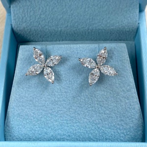 May include: A pair of silver flower-shaped earrings with clear marquise-shaped stones.