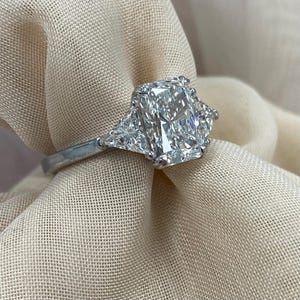 May include: A silver engagement ring with a large, rectangular, clear diamond in the center and two smaller, triangular, clear diamonds on either side.