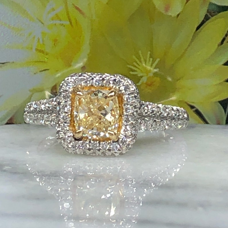 May include: A gold and white engagement ring with a large, cushion-cut, yellow diamond surrounded by a halo of smaller diamonds.