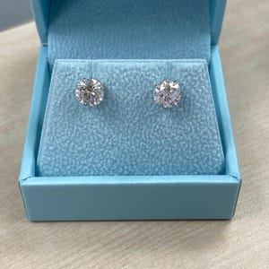 May include: A pair of diamond earrings in a light blue box. The earrings are round and have a silver setting.