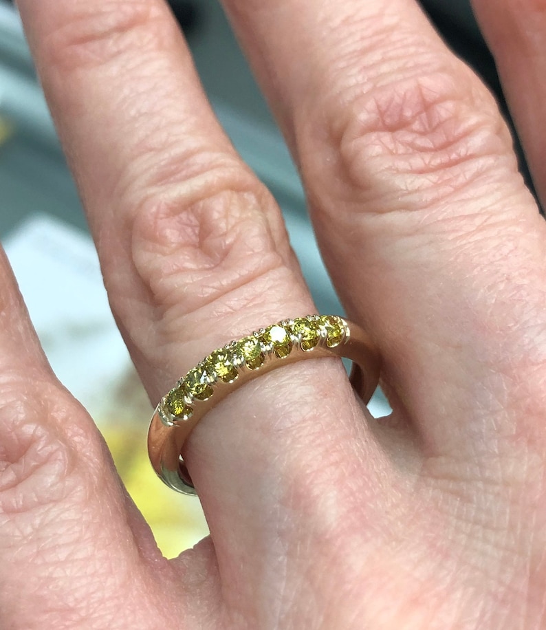 Puede incluir: Un anillo de banda de oro con una hilera de siete peque&ntilde;as piedras preciosas amarillas de corte redondo engastadas a lo largo de la mitad superior de la banda. El metal tiene un acabado pulido y las piedras est&aacute;n dispuestas en un engaste compartido.
