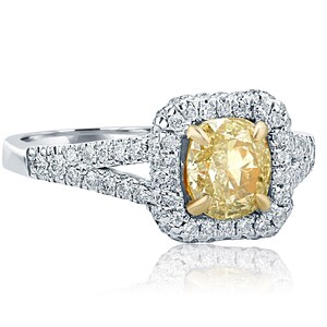 May include: A yellow gold and white gold engagement ring with a large, oval-shaped, yellow diamond center stone. The center stone is surrounded by a halo of smaller diamonds. The band is also set with smaller diamonds.