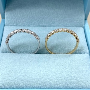 Pu&ograve; includere: Due fedi nuziali con diamanti, una in oro bianco e una in oro giallo, esposte in una scatola per anelli in velluto blu.