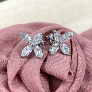 May include: A pair of silver flower-shaped earrings with clear, sparkling stones.