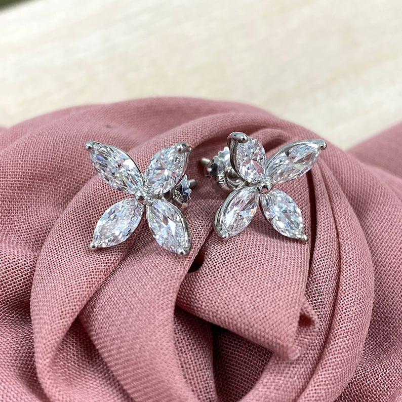 May include: A pair of silver flower-shaped earrings with clear, sparkling stones.
