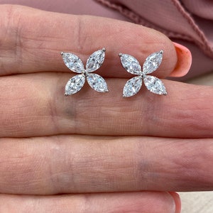 May include: A pair of silver earrings with a flower design featuring five clear marquise-shaped stones.