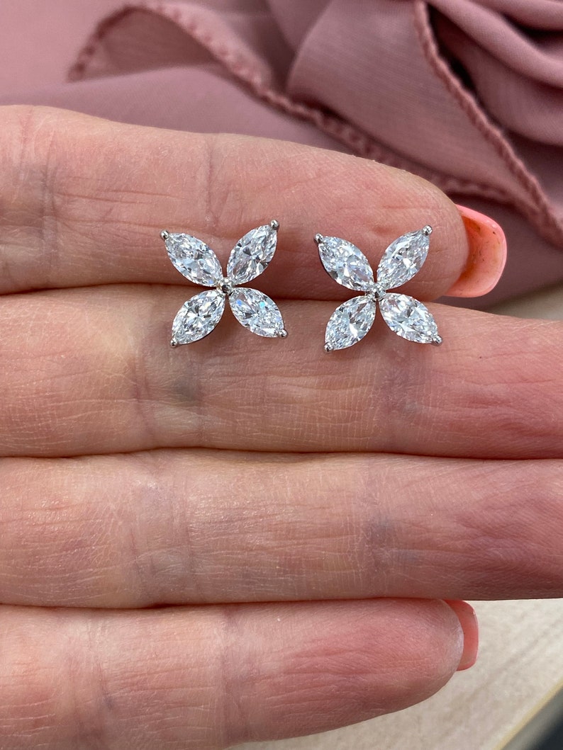 May include: A pair of silver earrings with a flower design featuring five clear marquise-shaped stones.