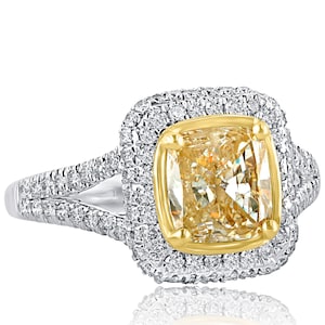 May include: A yellow diamond engagement ring with a cushion cut center stone surrounded by a double halo of smaller diamonds. The ring band is set with pave diamonds and has a split shank design.