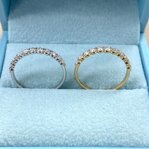 Pu&ograve; includere: Due fedi nuziali con diamanti, una in oro bianco e una in oro giallo, esposte in una scatola di velluto blu.